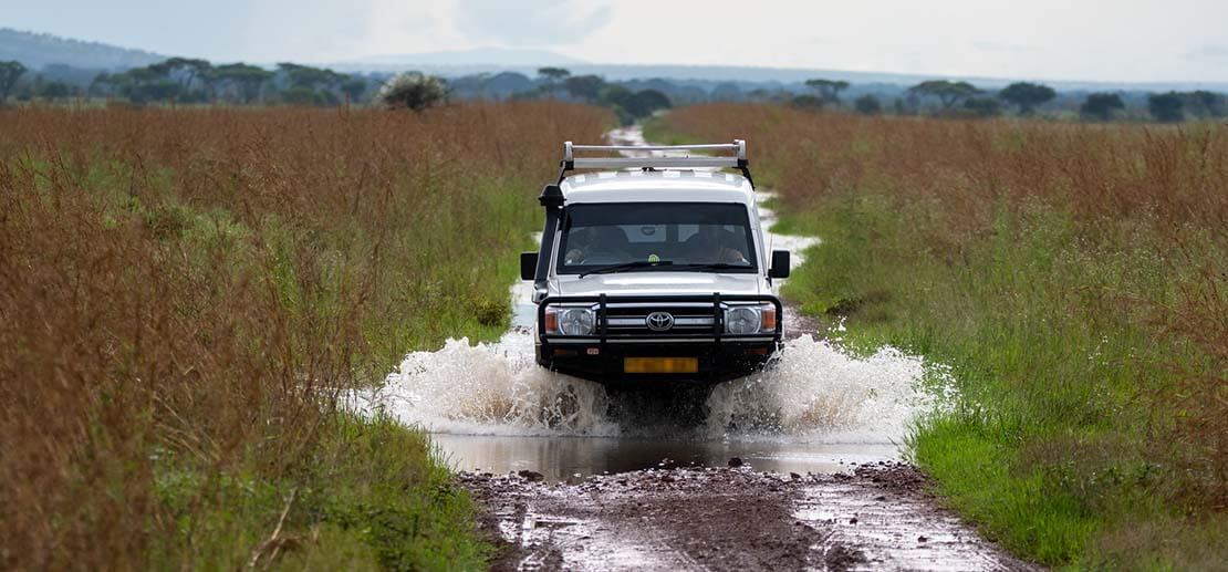 Safari vehicle crossing a small pool of water in a Tanzania National Park during a Mwewe Expeditions tour