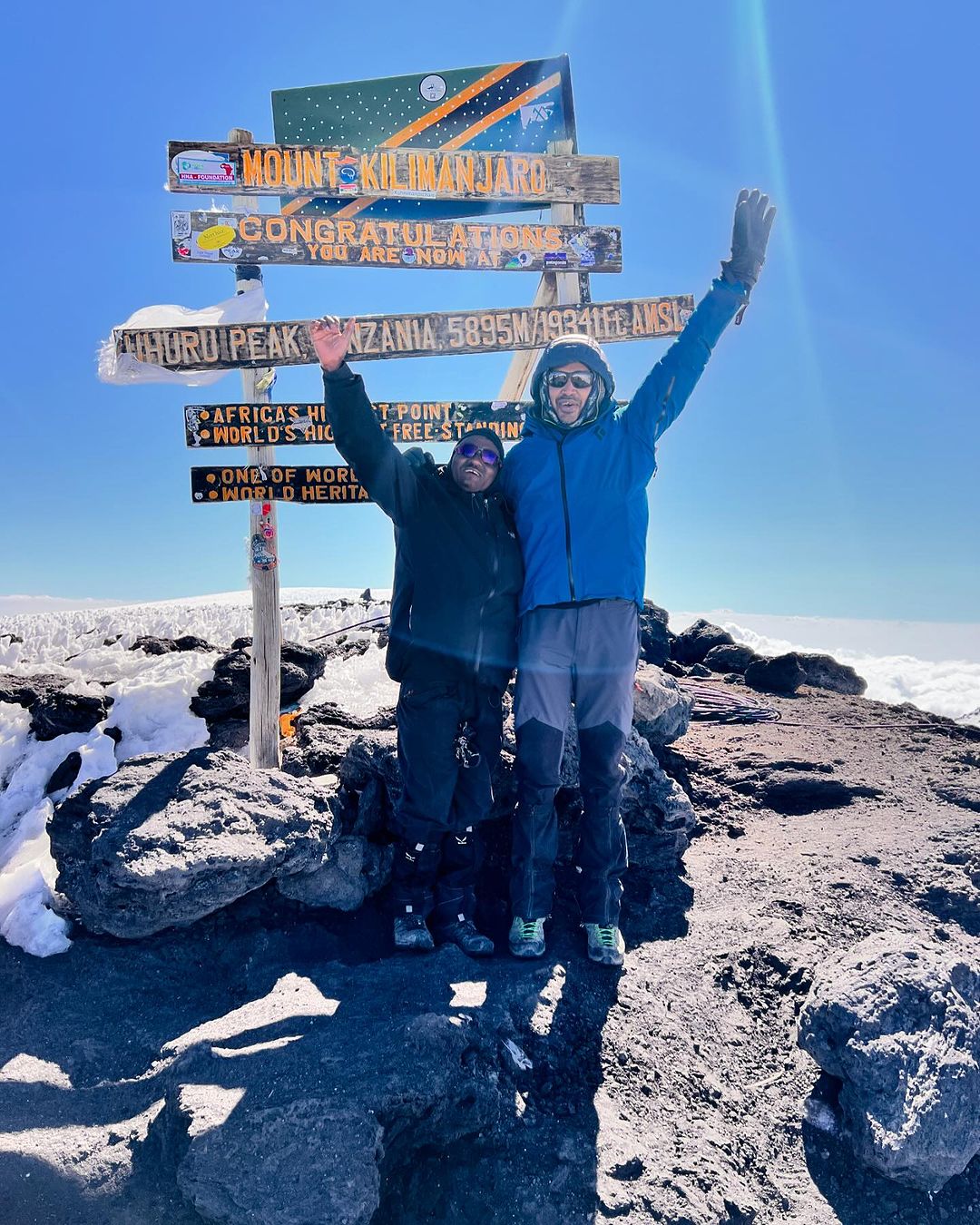 6. A traveler and a tour guide share a joyful moment at Uhuru Peak, 5,895m above sea level, with Mount Kilimanjaro\'s stunning summit in the background.