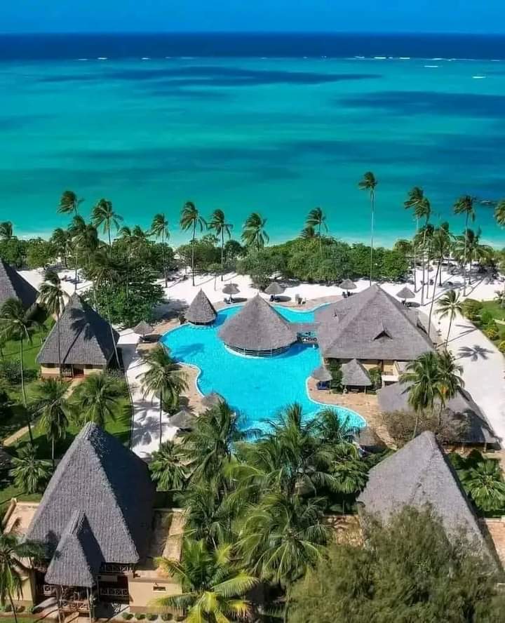 A stunning beach in Zanzibar with crystal-clear waters, soft white sands, and a luxury beachfront lodge surrounded by palm trees.